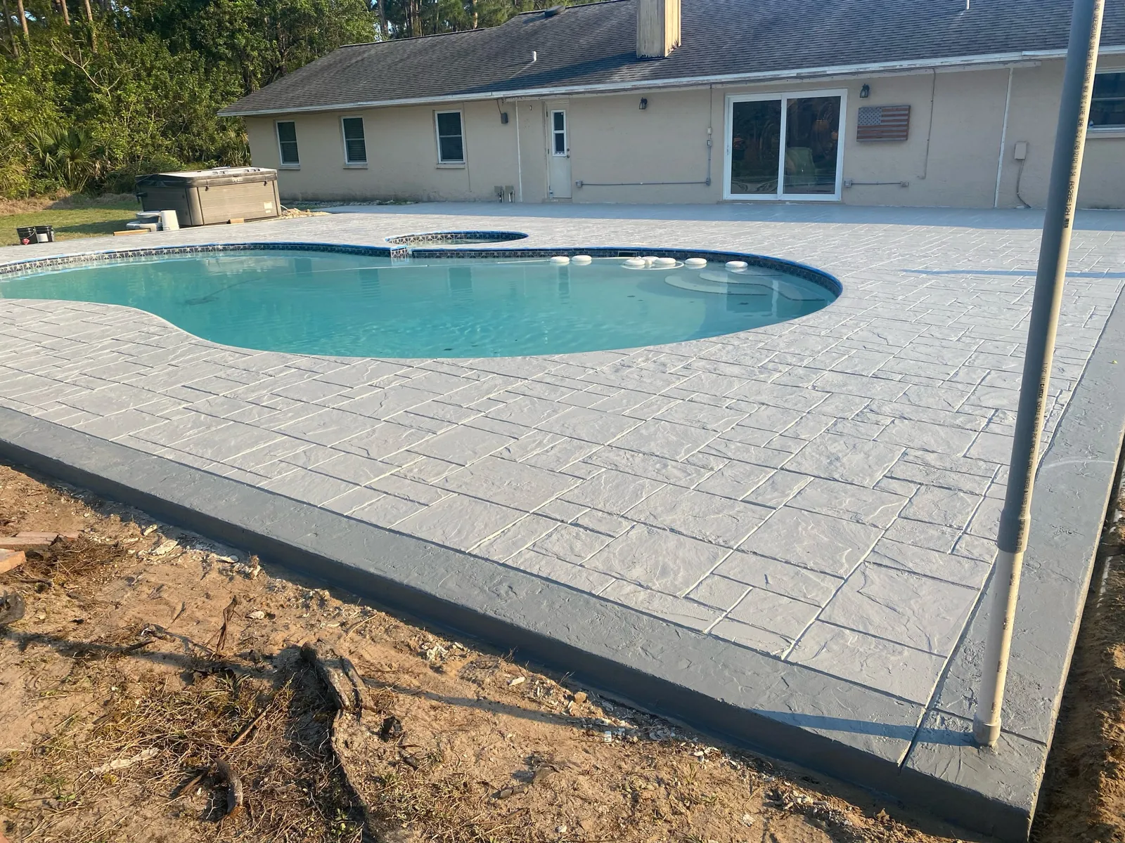 Gray ashlar stamped concrete pool deck around a backyard pool